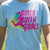 Girl wearing light blue soccer t-shirt featuring pink Girls With Goals slogan and player silhouette.