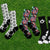 Six pairs of crew socks with soccer-themed patterns are arranged on a green grass background. The patterns include black and white soccer balls, red and white American flags, black and white soccer motifs, and red, white, and blue soccer balls and stars.
