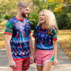 Pair wearing matching ugly Christmas sweater running outfits featuring blue holiday pattern t-shirts and red shorts.