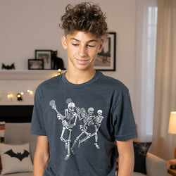 Youth wearing charcoal lacrosse t-shirt featuring a white graphic of three skeletons playing lacrosse.