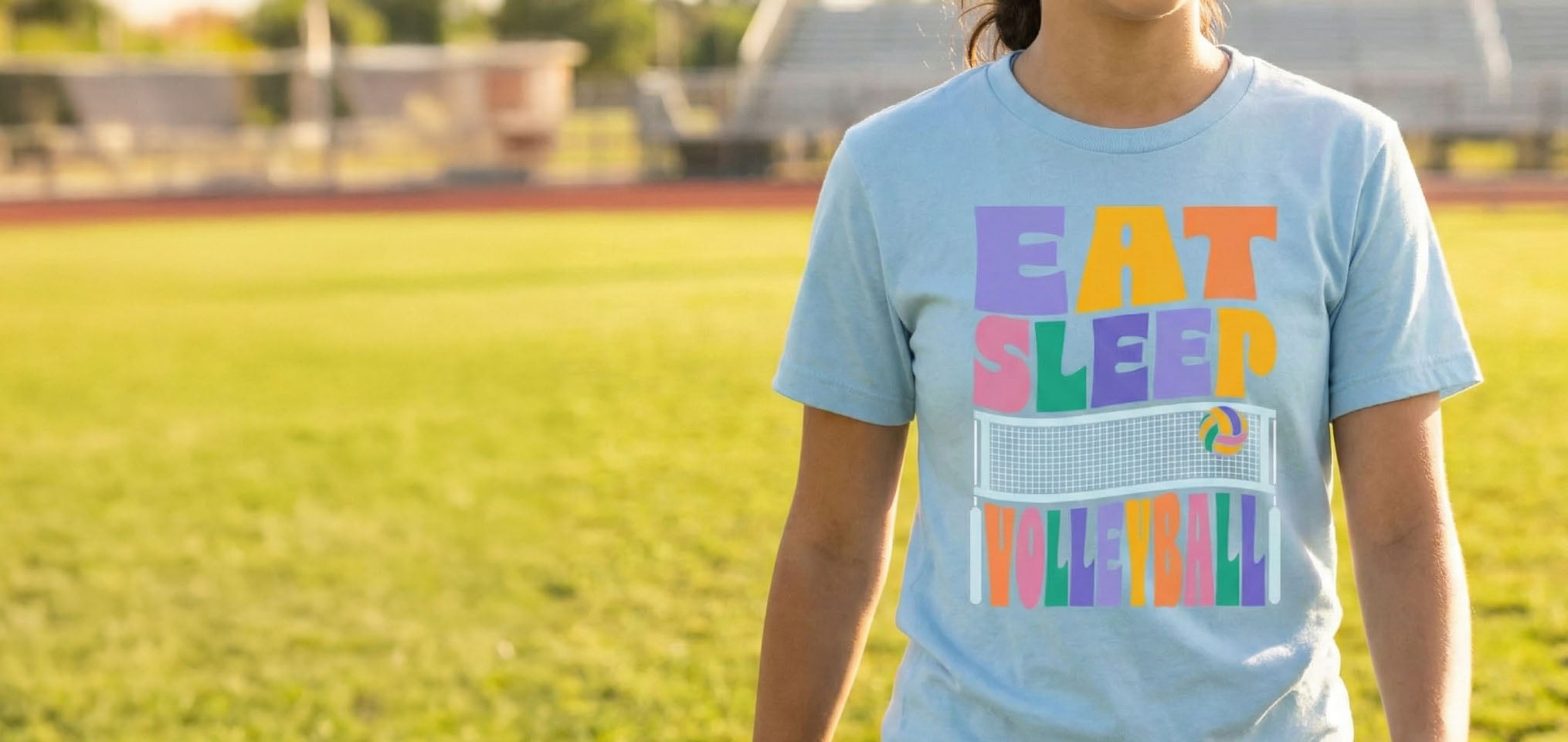 Girl wearing light blue volleyball t-shirt featuring colorful Eat Sleep Volleyball slogan and net graphic.
