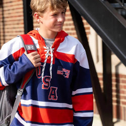 Youth wearing a red, white, and blue USA hockey lace-up hoodie featuring American flag graphic