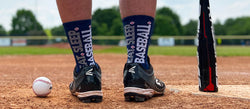 Player on a field wearing navy blue baseball socks featuring vertical Eat Sleep Baseball text on the back.