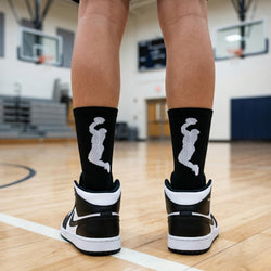 Person wearing black and white socks  with basketball player graphic in a gymnasium.
