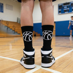 Person wearing black socks with basketball designs and black and white sneakers on a gymnasium floor.