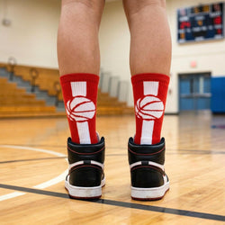 Person wearing red socks with basketball designs on a gymnasium floor.