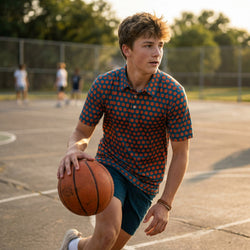 Young man wearing a basketball patterned polo on an outdoor court with trees in the background
