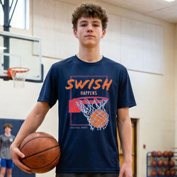 Person wearing a navy blue t-shirt with 'SWISH HAPPENS' design, holding a basketball in an indoor sports facility.