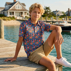 Young man wearing a basketball polo shirt sitting on a dock by a waterfront with a house and boat in the background