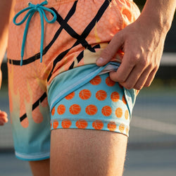Person wearing colorful shorts with a basketball pattern, standing on a blurred background.