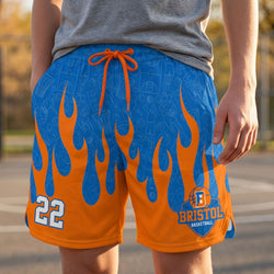 Orange and blue basketball shorts with flame design and 'Bristol Basketball' logo on a blurred outdoor background