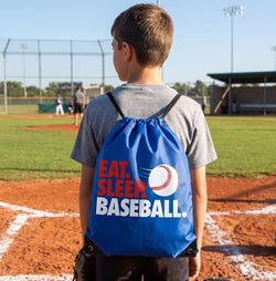 Child with a blue drawstring bag that says 'Eat. Sleep. Baseball.' on a baseball field.