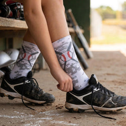 Person wearing baseball-themed camo socks and cleats on a sports field.