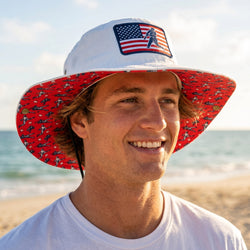 Man wearing a red and white bucket hat with an American flag design on a beach.