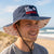 Man wearing a bucket hat with 'Eat. Sleep. Baseball' text on a beach.