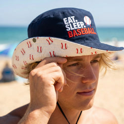 Person wearing a cap with 'Eat. Sleep. Baseball' text on a beach