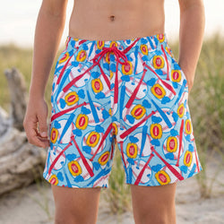 Boy wearing baseball swim trunks on a grassy beach