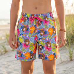 Person wearing colorful tropical-themed baseball swim trunks on a beach.