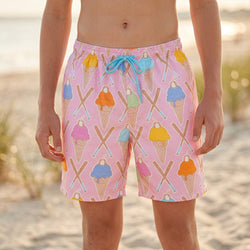 Person wearing pink swim trunks with ice cream cone and baseball bat pattern on a beach.