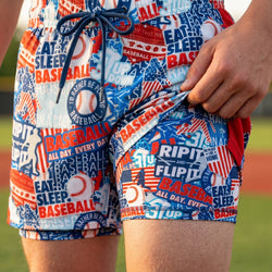 Colorful baseball-themed shorts with text and graphics on a blurred sports field background.