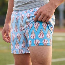 Person wearing blue shorts with baseball and ice cream cone pattern on a sports field.