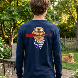 Person wearing a navy blue long-sleeve shirt with a graphic of a dog holding an American flag and a baseball bat, standing in a garden.