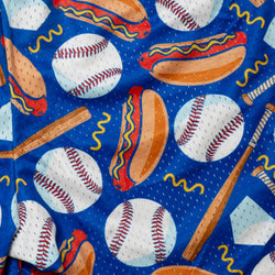 A close-up of a blue fabric with a baseball-themed print featuring white baseballs with red stitching, hot dogs with mustard, wooden bats, and yellow wavy lines.