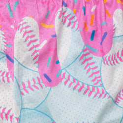 A close-up of a pink and white patterned fabric featuring baseballs with colorful sprinkles, including blue, orange, yellow, and purple accents.