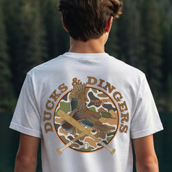 A boy viewed from behind wearing a white t-shirt with a large graphic on the back. The graphic features a duck hunting theme with crossed baseball bats, camouflage circle, and the text 'DUCKS & DINGERS' and 'HUNTING CLUB'.