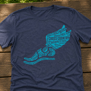 A navy blue heathered t-shirt laid flat on a rustic wooden surface, featuring a graphic of winged run shoe filled with running and cross-country training words in bright teal.
