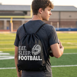 Person with a 'Eat. Sleep. Football.' drawstring backpack on a football field