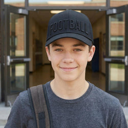 Young man wearing a black 'FOOTBALL' cap in front of a building entrance.