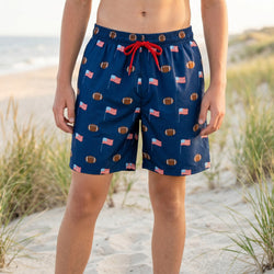 Person wearing blue swim trunks with football and usa flag pattern on a beach.