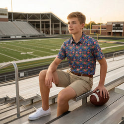 Young man wearing a football and floral patterned polo shirt sitting on bleachers at a football field holding a football.