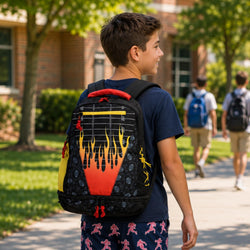 A boy wearing a black backpack with a red, orange, and yellow flame design walks on a sunny school campus path. Other students are visible in the background.
