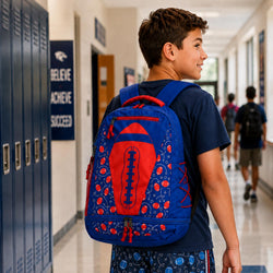 A boy wearing a blue and red patterned backpack with a football design, photographed in a school hallway.