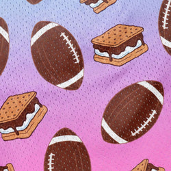 A close-up of a fabric pattern featuring brown American footballs and graham cracker s'mores on a pink and purple mesh background.