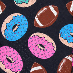 A close-up of a fabric pattern featuring pink and blue frosted donuts with sprinkles and brown footballs on a black micro-dot background.