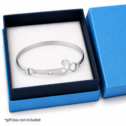 A polished silver-toned metal bangle bracelet displayed inside an open blue gift box with a white insert. The bracelet has a smooth curved band with a sliding clasp and a small decorative ring detail.