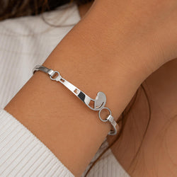 A polished silver-tone metal bracelet with a field hockey stick head design, shown worn on a person's wrist.