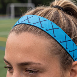 Person wearing a blue headband with black field hockey stick patterns on a blurred field background