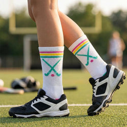Person wearing white socks with colorful field hockey design and black sports shoes on a grassy field.
