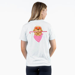 A woman shown from the back wearing a white t-shirt with a graphic of a golden retriever wearing orange sunglasses and a pink bandana, holding a pink field hockey stick.