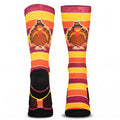 A pair of crew socks with a Thanksgiving theme, featuring a cartoon turkey wearing a pilgrim hat on a background of horizontal orange, yellow, and burgundy stripes, with a black foot section.