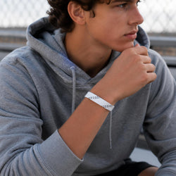 A man wearing a gray hoodie and black shorts, looking off-camera while wearing a white wristband with small black printed dots on his wrist.