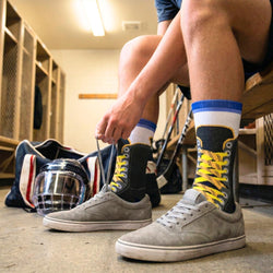Person tying shoelaces in a locker room with colorful hockey lace socks and sports equipment.