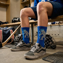Person wearing blue socks with yeti hockey design in a locker room setting.