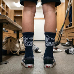 Person wearing black socks with 'I'd Rather Be Playing Hockey' text in a locker room.