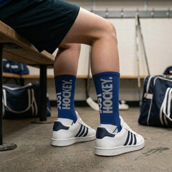 Person wearing blue hockey socks with 'Hockey' text, sitting on a bench in a locker room.