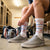 Person sitting in a locker room wearing gray sneakers and white socks with red and blue hockey rink design.